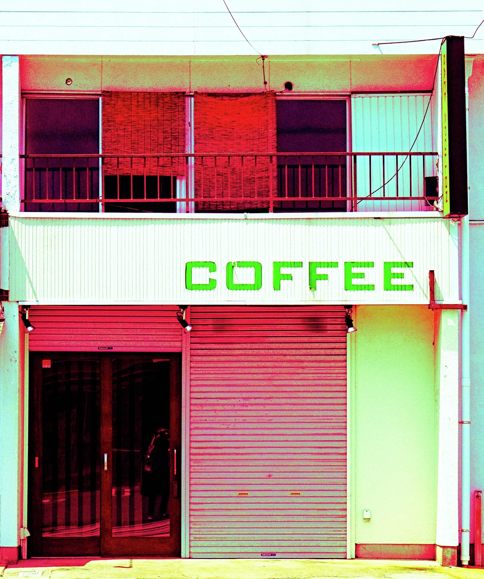 Green COFFEE lettering tops red shutters beneath a balcony with red window panels.