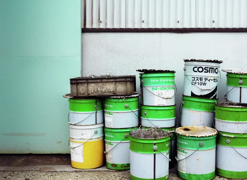 Stacks of green and white metal buckets stand against a pale wall beside a turquoise door.