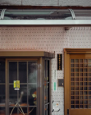 A curved transparent canopy extends above a tiled facade with sliding windows and a wooden lattice door.