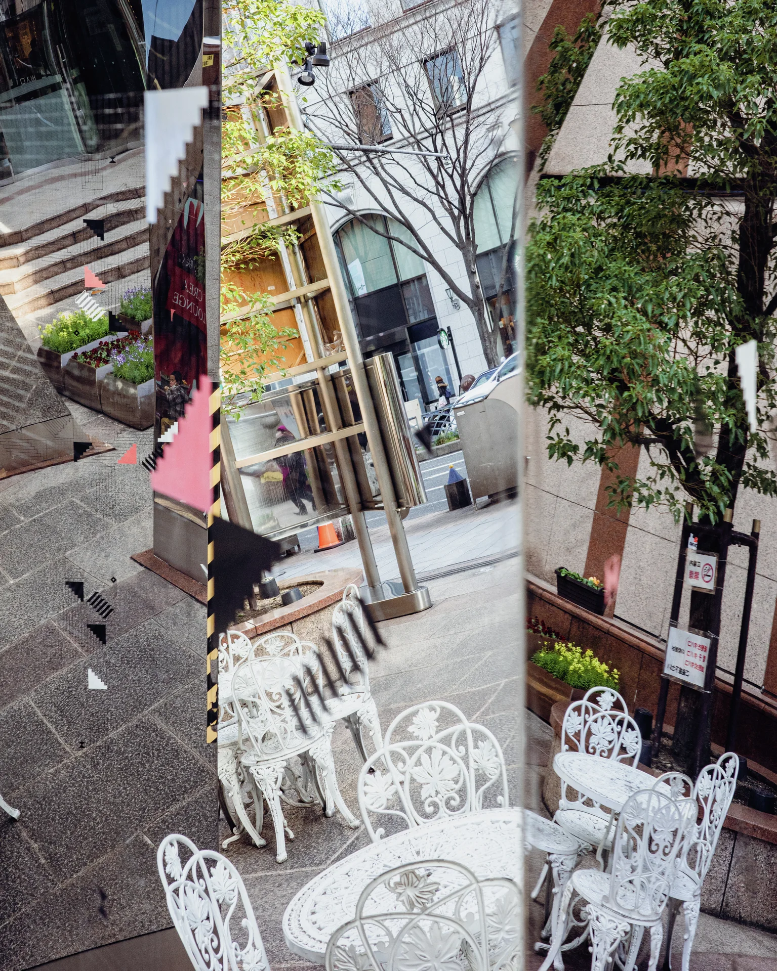 Tall reflective panels fragment a courtyard scene of white metal chairs, tables, trees, and nearby buildings.