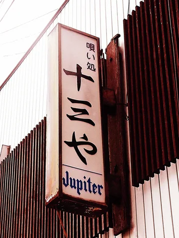 Black Japanese characters and Jupiter lettering fill a weathered projecting sign beside vertical wooden slats.