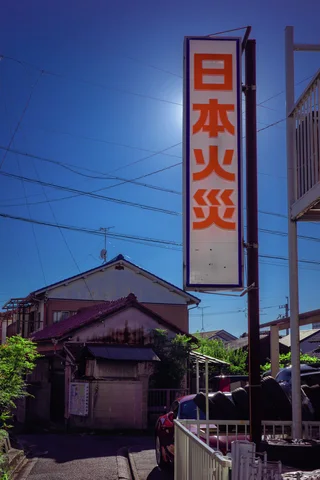 A tall white sign with red Japanese lettering rises above low buildings beneath blue sky.