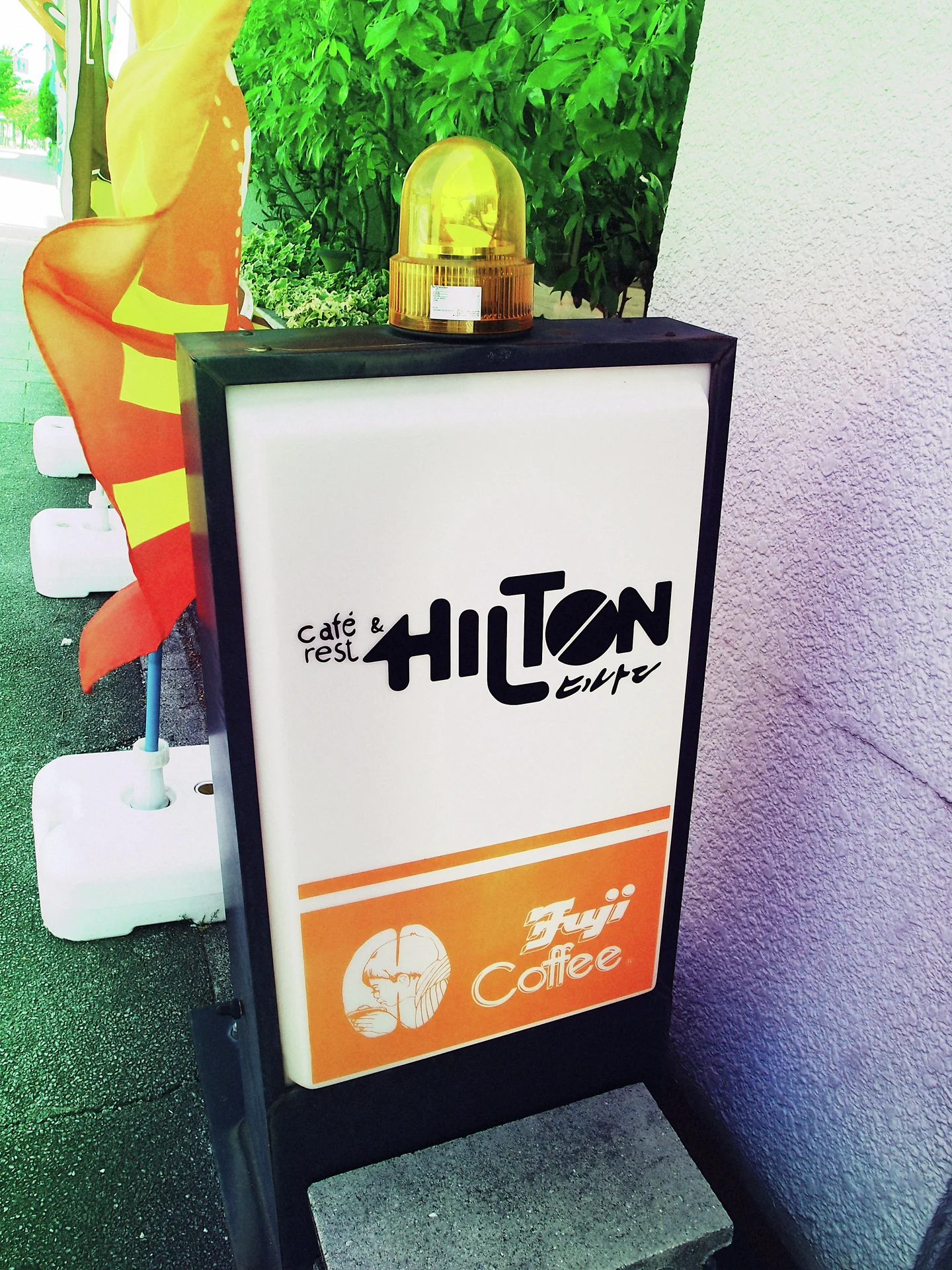 A black-framed cafe sign with an orange lower panel stands beneath a small yellow beacon.