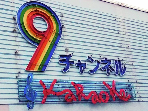 A rainbow-striped number nine hangs above blue Japanese letters and red Karaoke script on pale siding.
