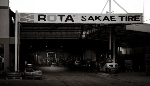 A large tire shop canopy shelters stacked tires and a small vehicle in black and white.