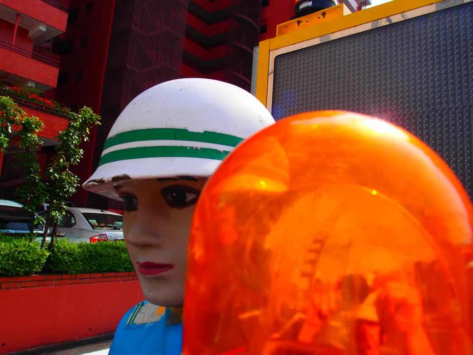 An orange beacon fills the foreground beside a mannequin's face and green-striped white helmet.