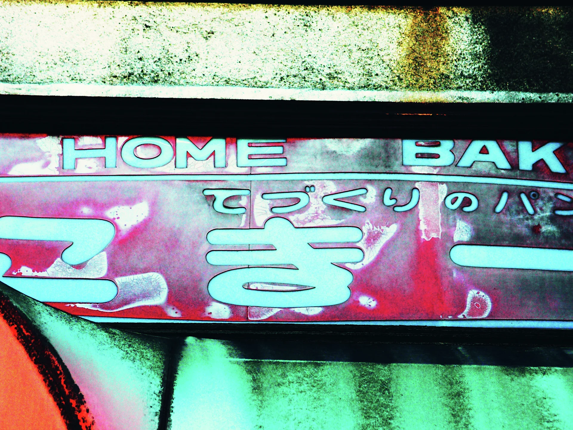 A peeling red bakery sign with pale English and Japanese lettering sits beneath a stained concrete ledge.