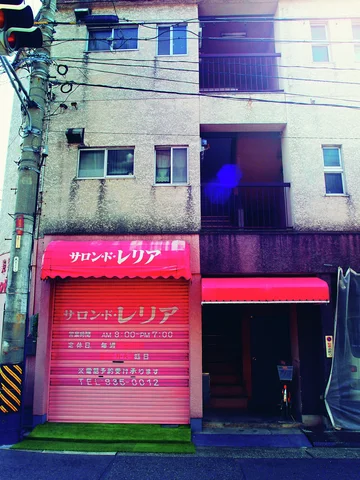 Pink salon shutters and a red awning brighten the ground floor of a gray apartment building.