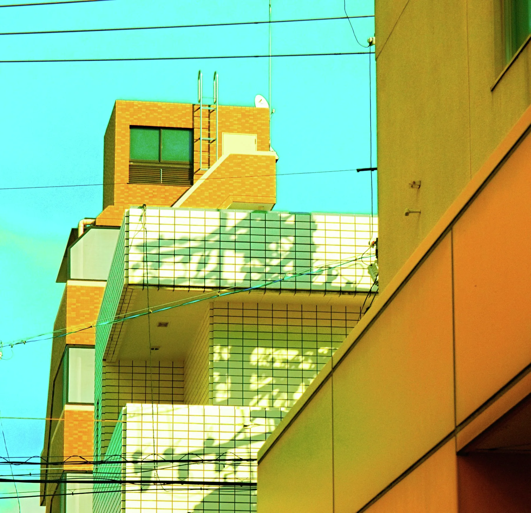 An exterior staircase casts angular shadows across a tiled building beside an orange wall under turquoise sky.