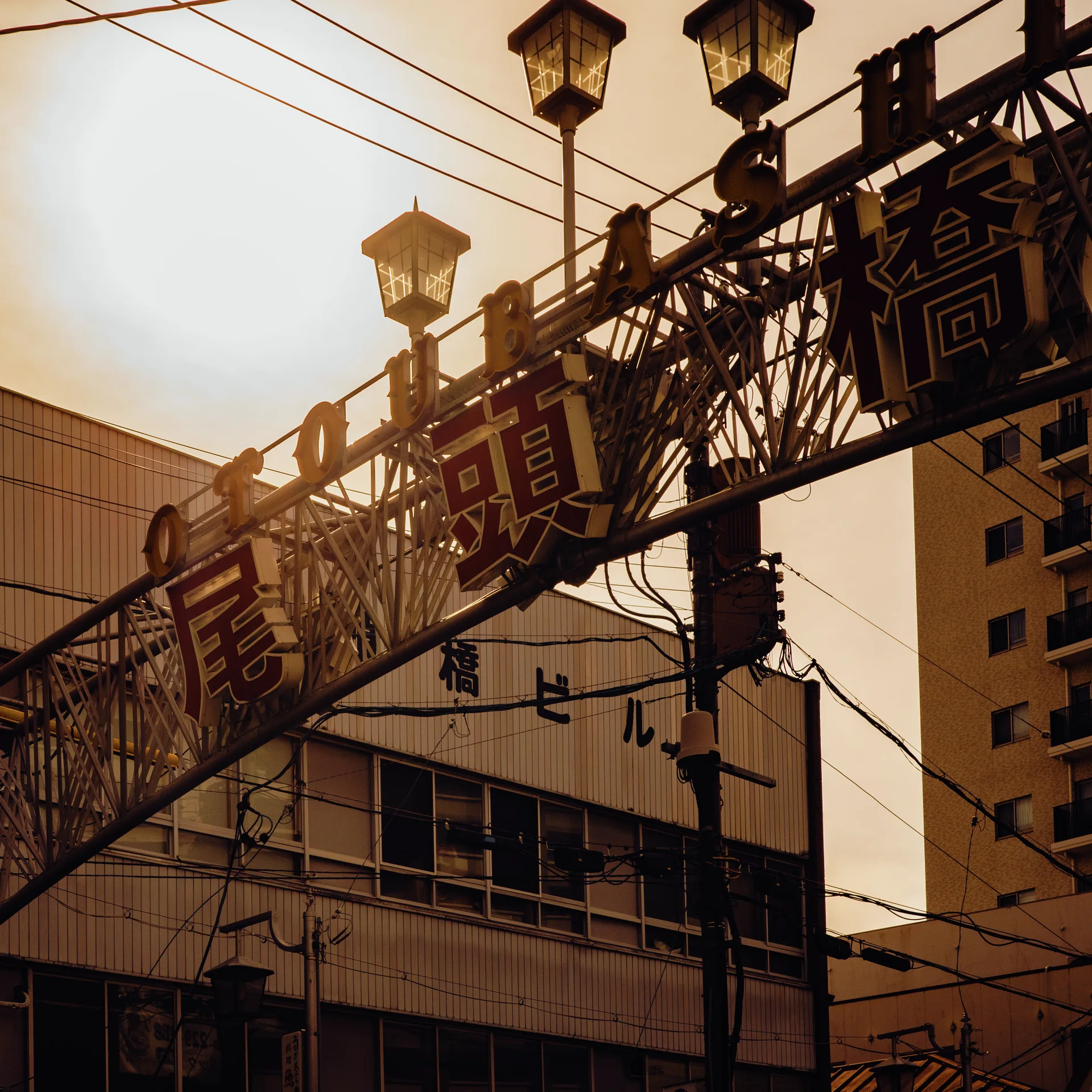 An ornate overhead street arch carries Japanese signs and lanterns among utility wires and surrounding buildings.