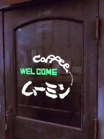 White Coffee script and Japanese lettering surround green WELCOME text on a dark wooden door.