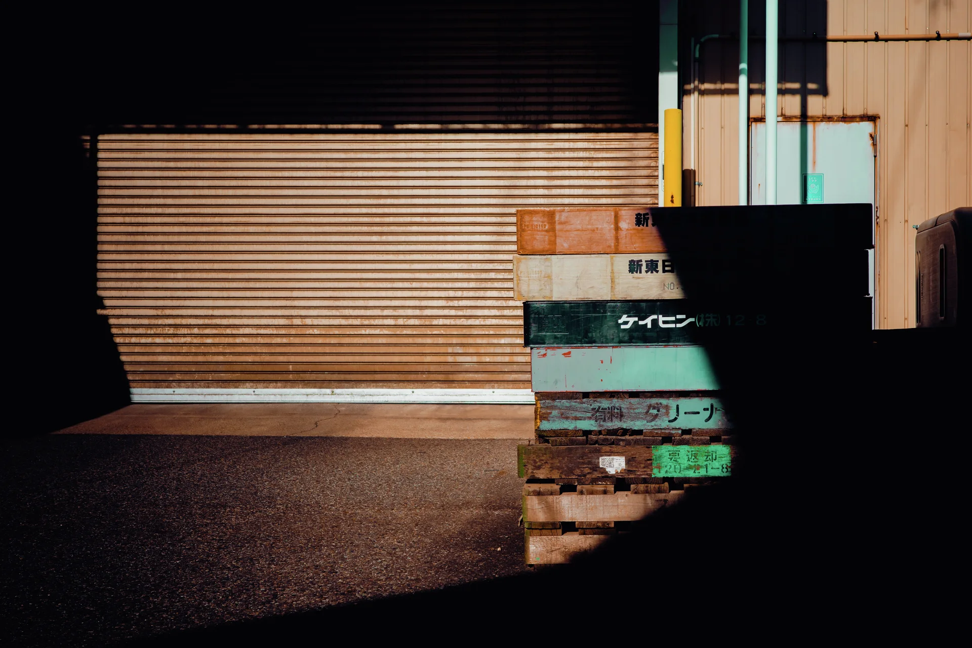 Sunlight forms a broad bright patch across a closed shutter beside stacked weathered wooden pallets.