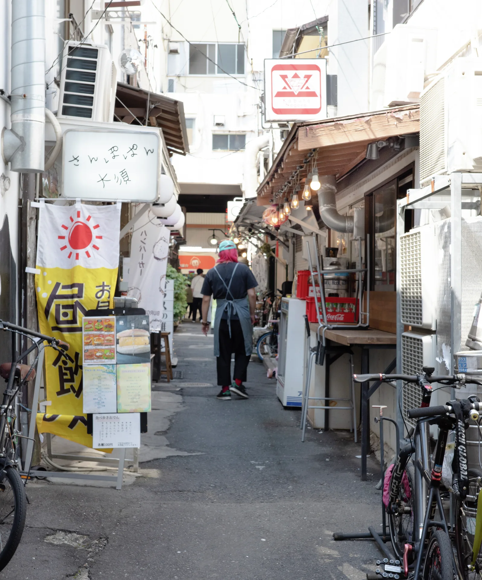 A person stands in a narrow shop-lined passage with hanging signs and bicycles parked along one wall.