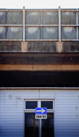 A blue right-arrow sign stands before a pale doorway beneath a tall row of weathered windows.