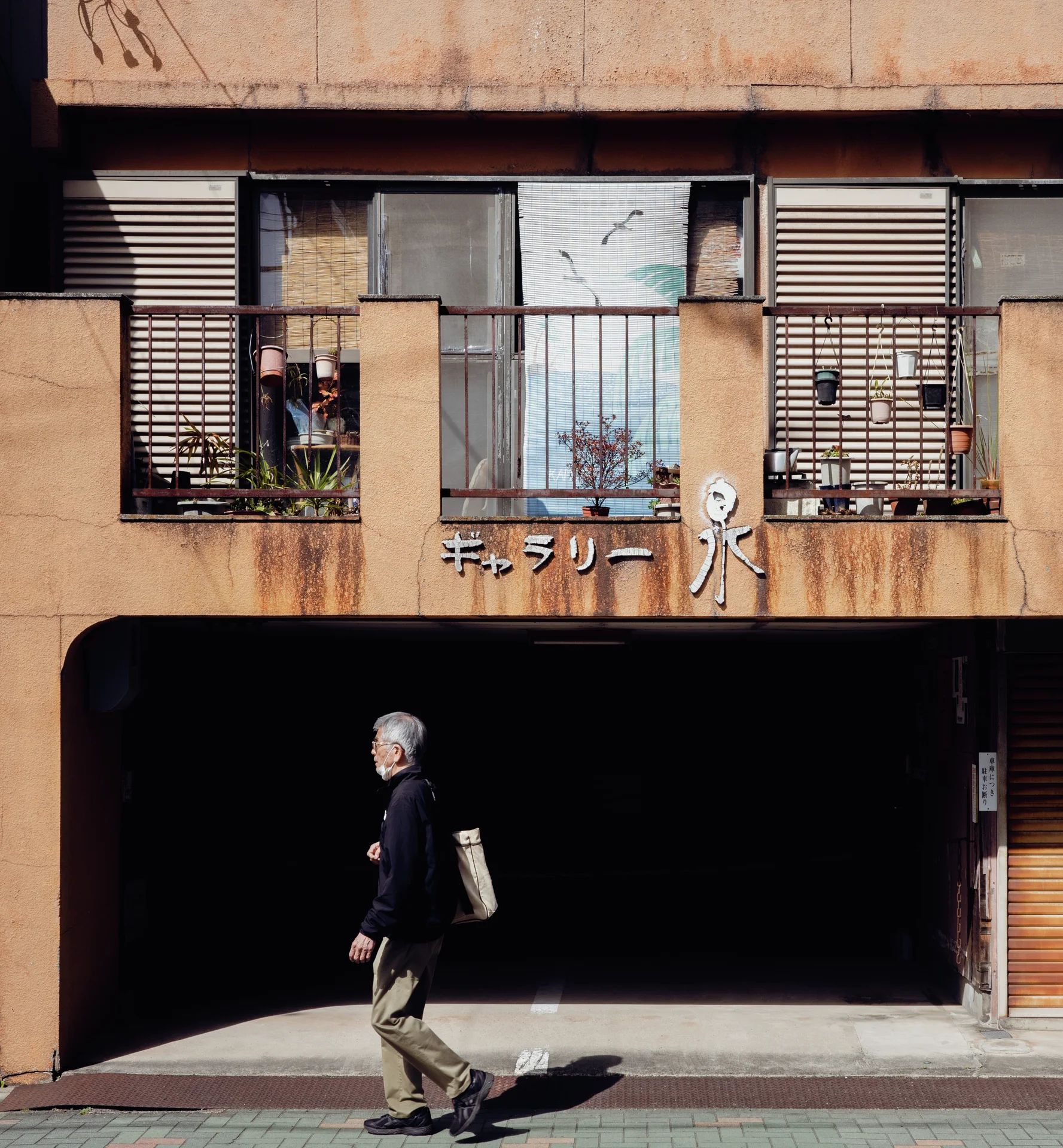 A pedestrian walks past a recessed entrance beneath a stained facade with barred upper windows.