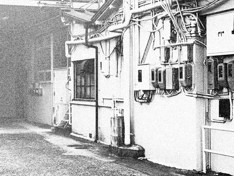 Dense cables and utility meters cover a pale wall beside a gritty monochrome alley.