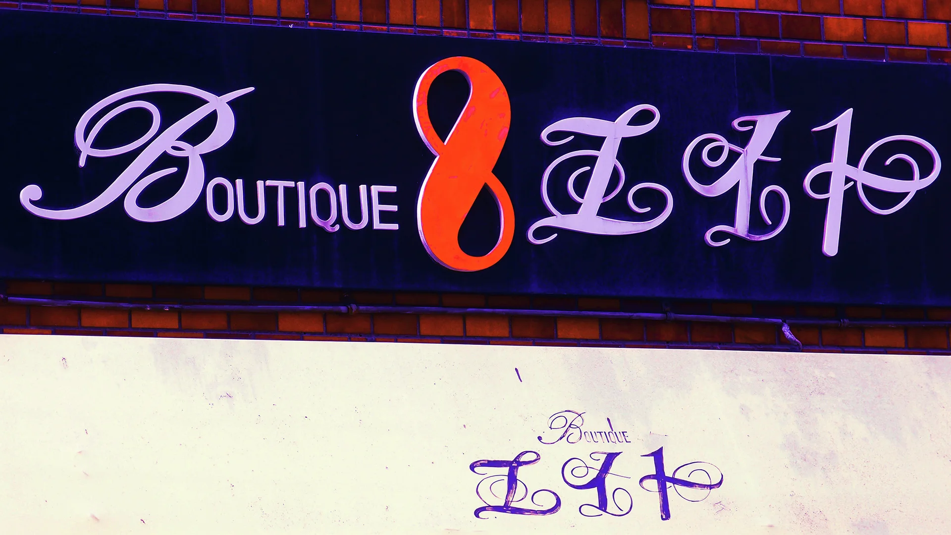 Ornate pale boutique lettering surrounds a large orange figure eight on a dark sign.