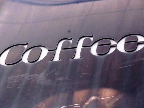 Pale italic Coffee lettering stretches across a scratched dark metal panel viewed at an angle.