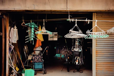Empty clothes hangers dangle across an open storage entrance containing bicycles, bags and assorted tools.
