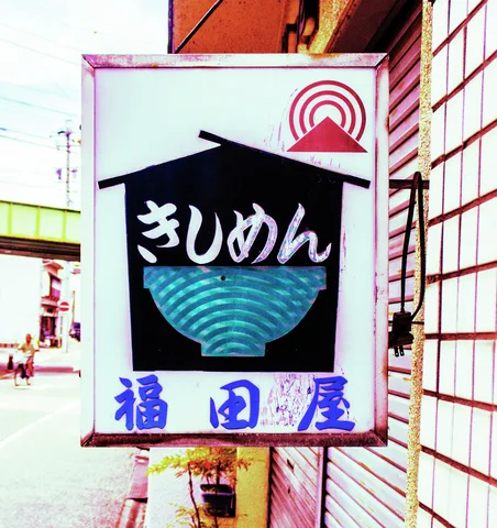 A projecting white sign displays a blue bowl beneath Japanese lettering and a dark house-shaped graphic.