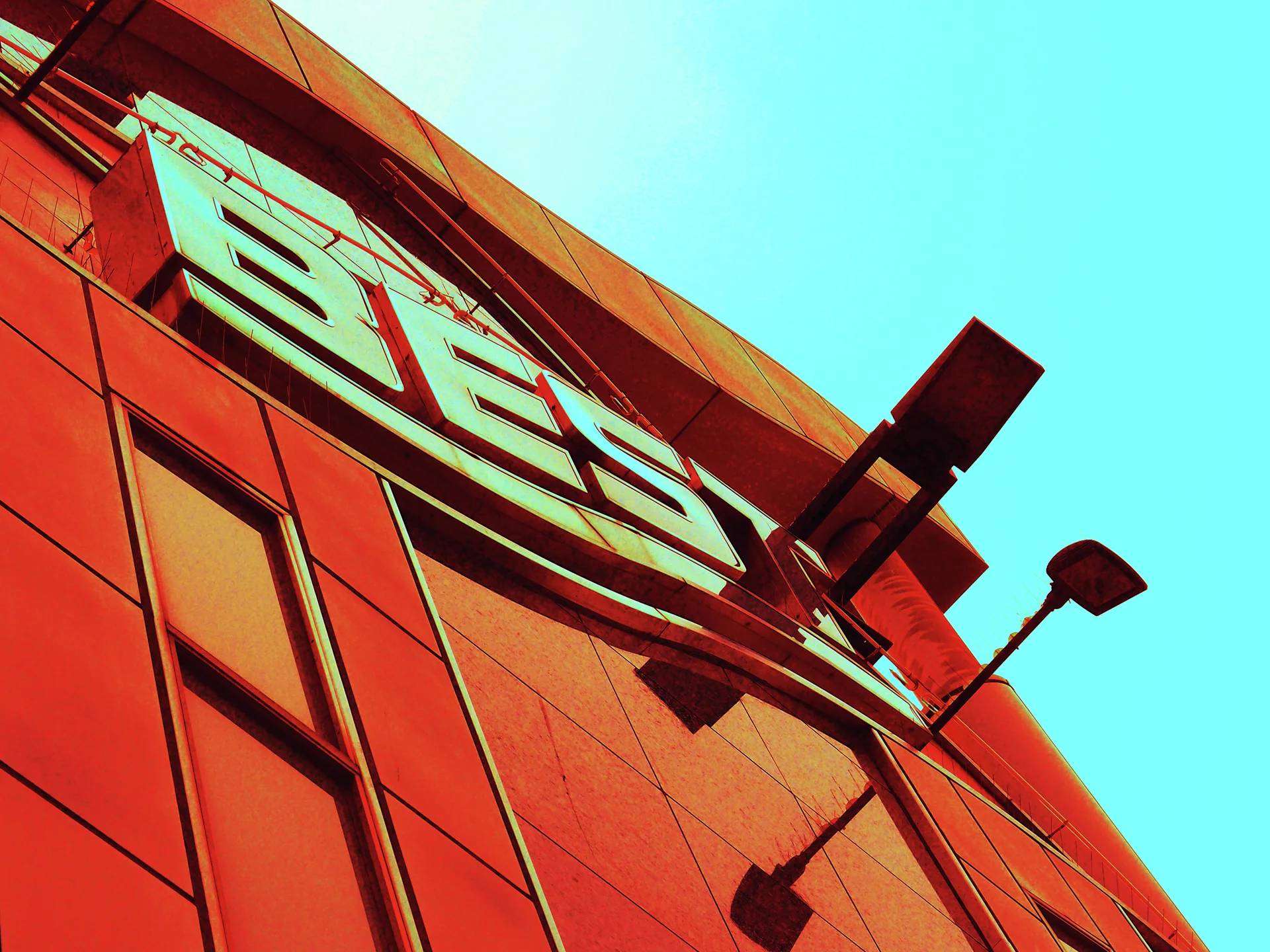 Large pale lettering and two projecting lamps stand against a vivid orange building and turquoise sky.