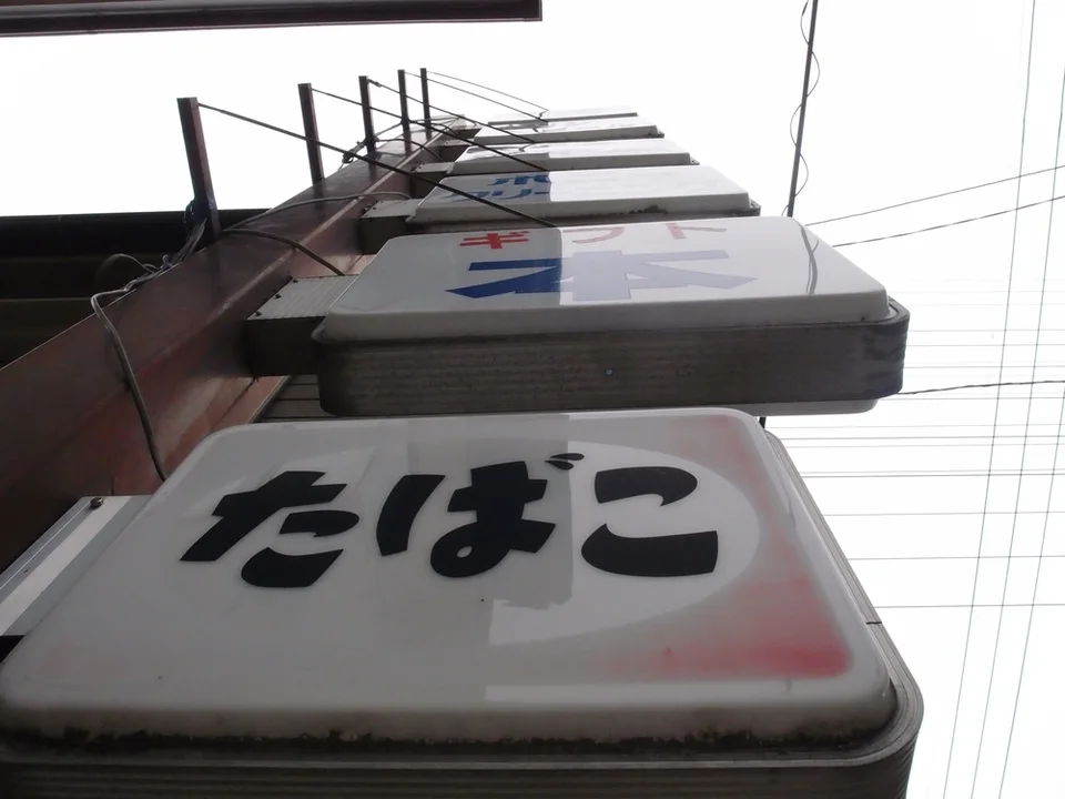 Projecting pale business signs climb a building viewed from below beneath a mesh of overhead wires.