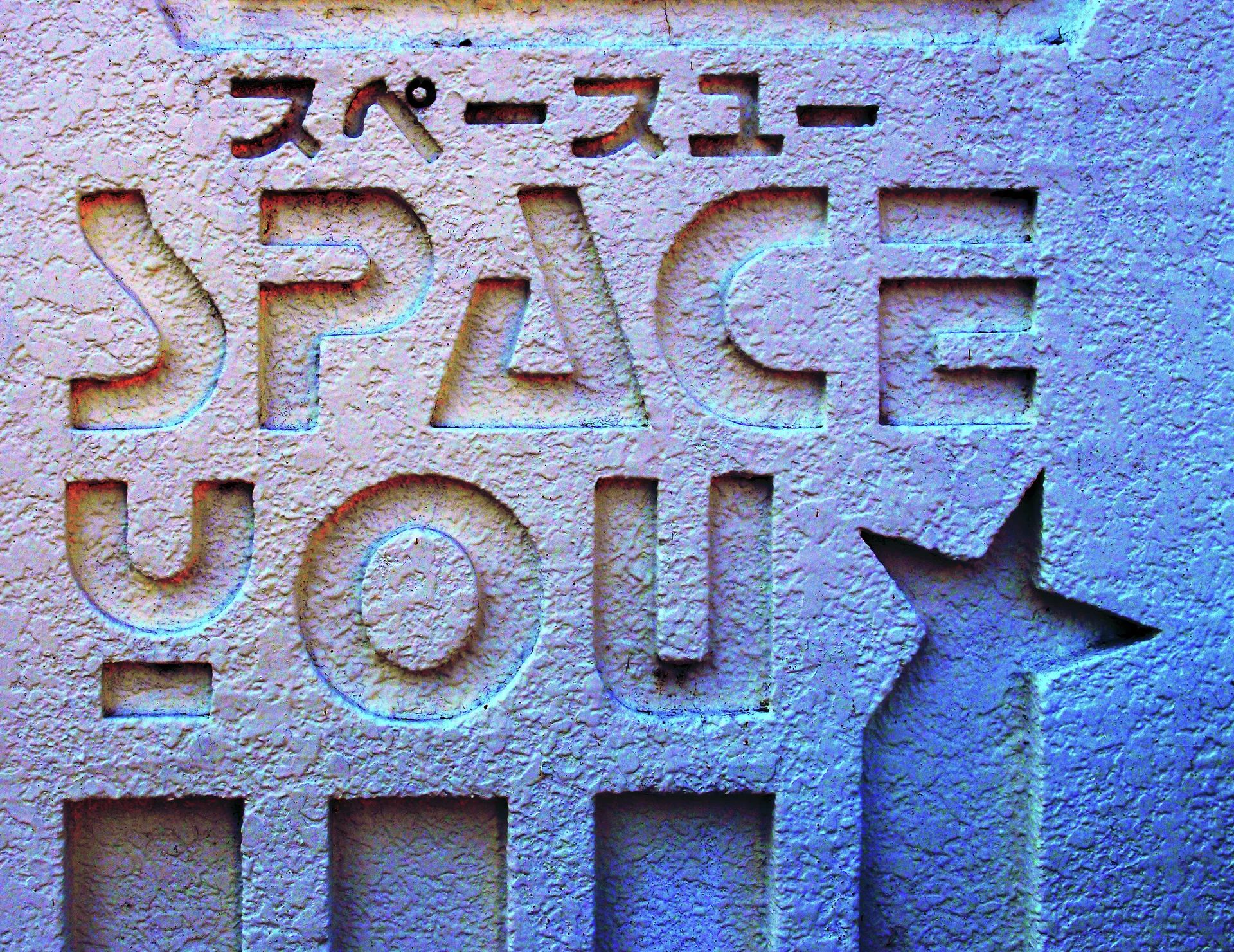 Carved Space You lettering and a star motif mark a rough pale wall with small square recesses.