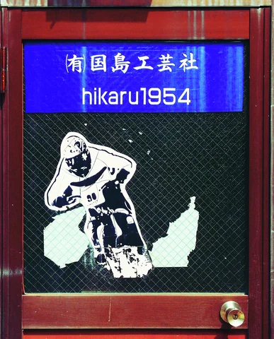 A peeling white guitarist illustration covers a mesh-glass door beneath a blue sign reading hikaru1954.