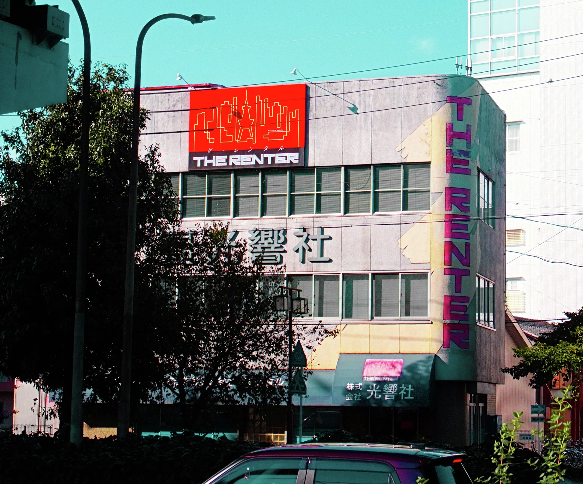 Large red signage crowns a pale multi-story building partly hidden by a leafy tree and parked car.