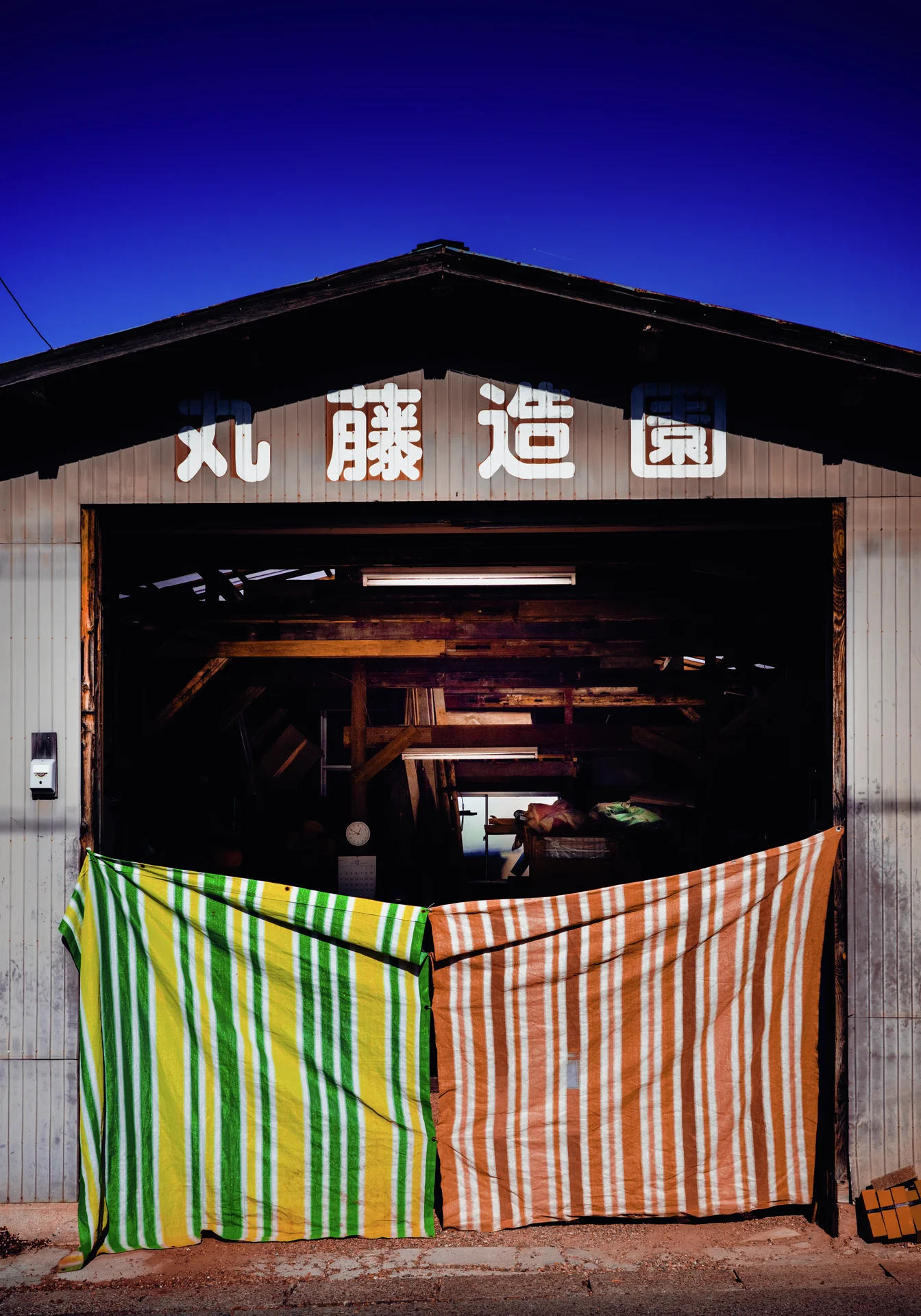 Green-yellow and pink striped fabric closes the lower opening of a dark wooden workshop entrance.