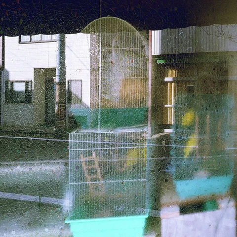 Textured glass overlays a street view with a wire cage, pale buildings, and turquoise reflections.