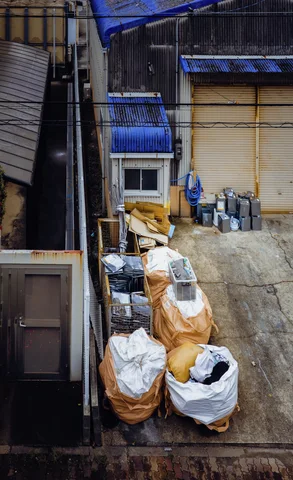 Bulging white and tan sacks line a narrow concrete space beside a closed yellow shutter.