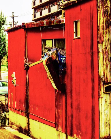 A torn window opening exposes bundled material through a weathered red metal wall.