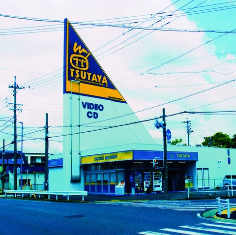 A triangular TSUTAYA tower sign rises above a low storefront beneath crossing utility wires.