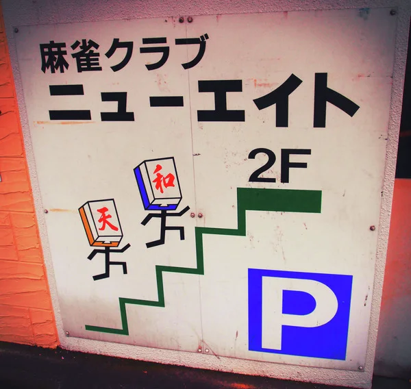 A pale sign shows black characters, cartoon game tiles, green stairs, and a blue parking symbol.