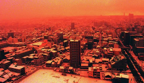 An orange cast covers dense city buildings and pale snow-covered ground beneath a hazy horizon.