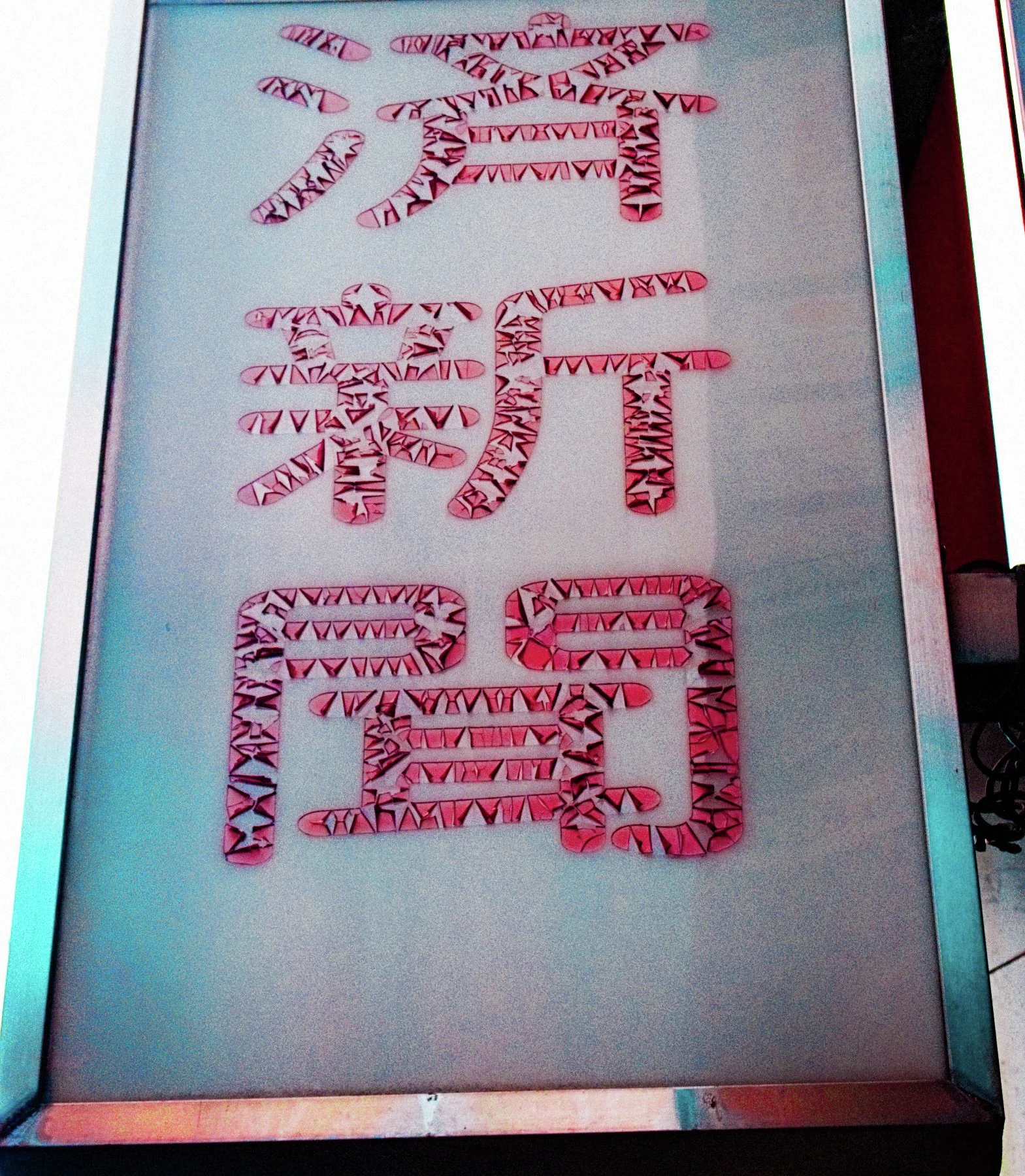 Large red patterned characters fill a tall pale sign within a thin dark frame.