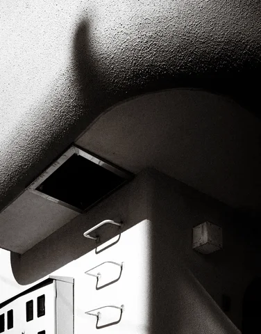 A curved textured overhang and small metal loops cast sharp shadows in black and white.