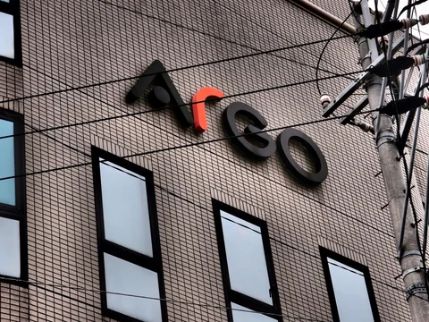 Raised dark lettering and an orange accent decorate a tiled building crossed by utility wires.