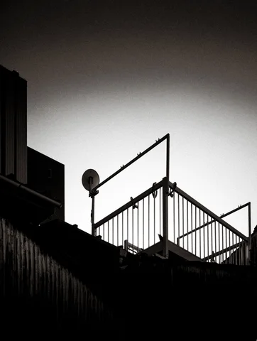 A rooftop railing and small satellite dish silhouette against a pale monochrome sky.