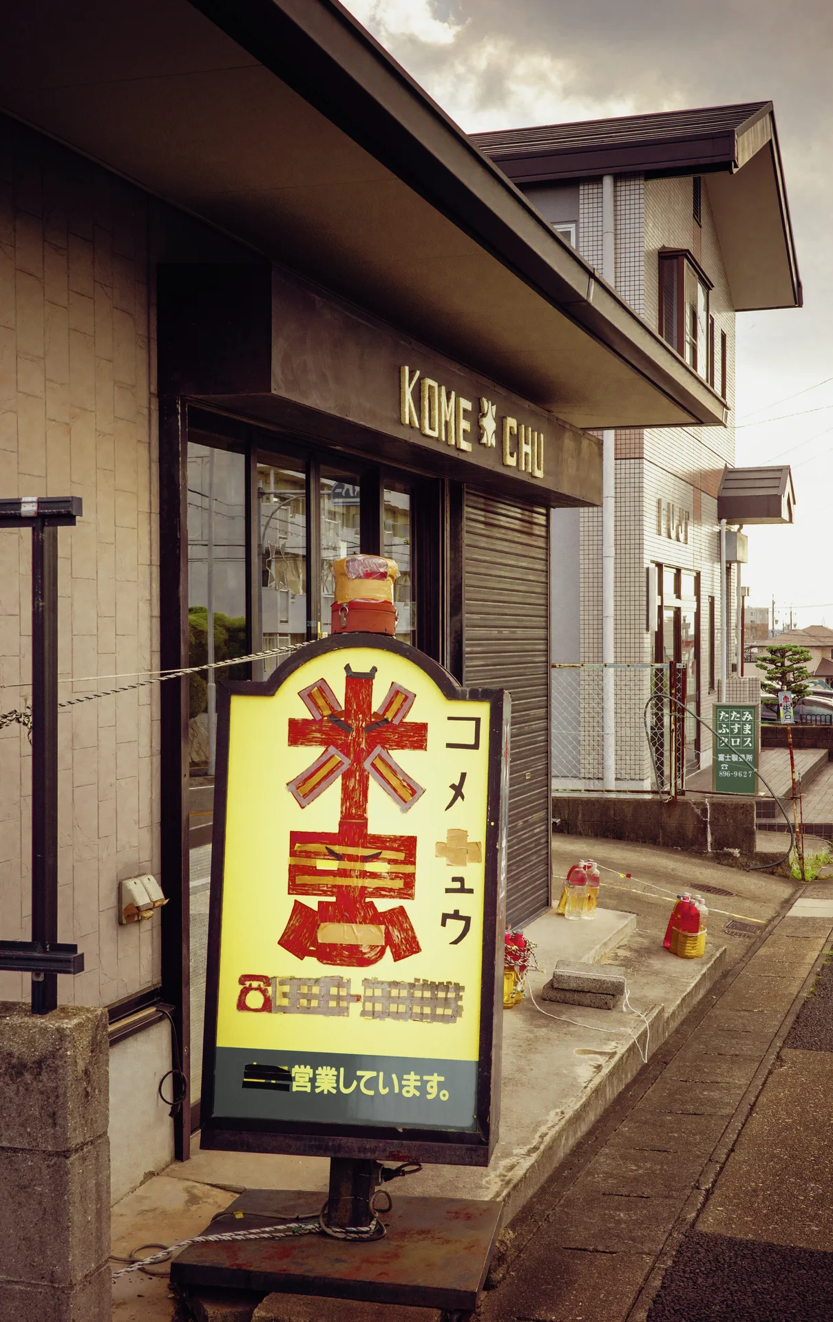 A freestanding yellow sign with large red characters stands outside a small street-side shop.