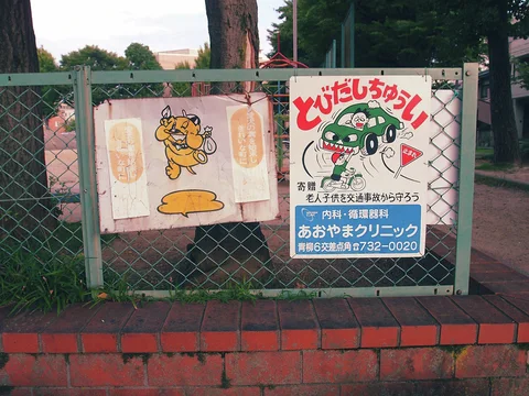 Two colorful cartoon posters hang on a chain-link fence above a low red brick wall.
