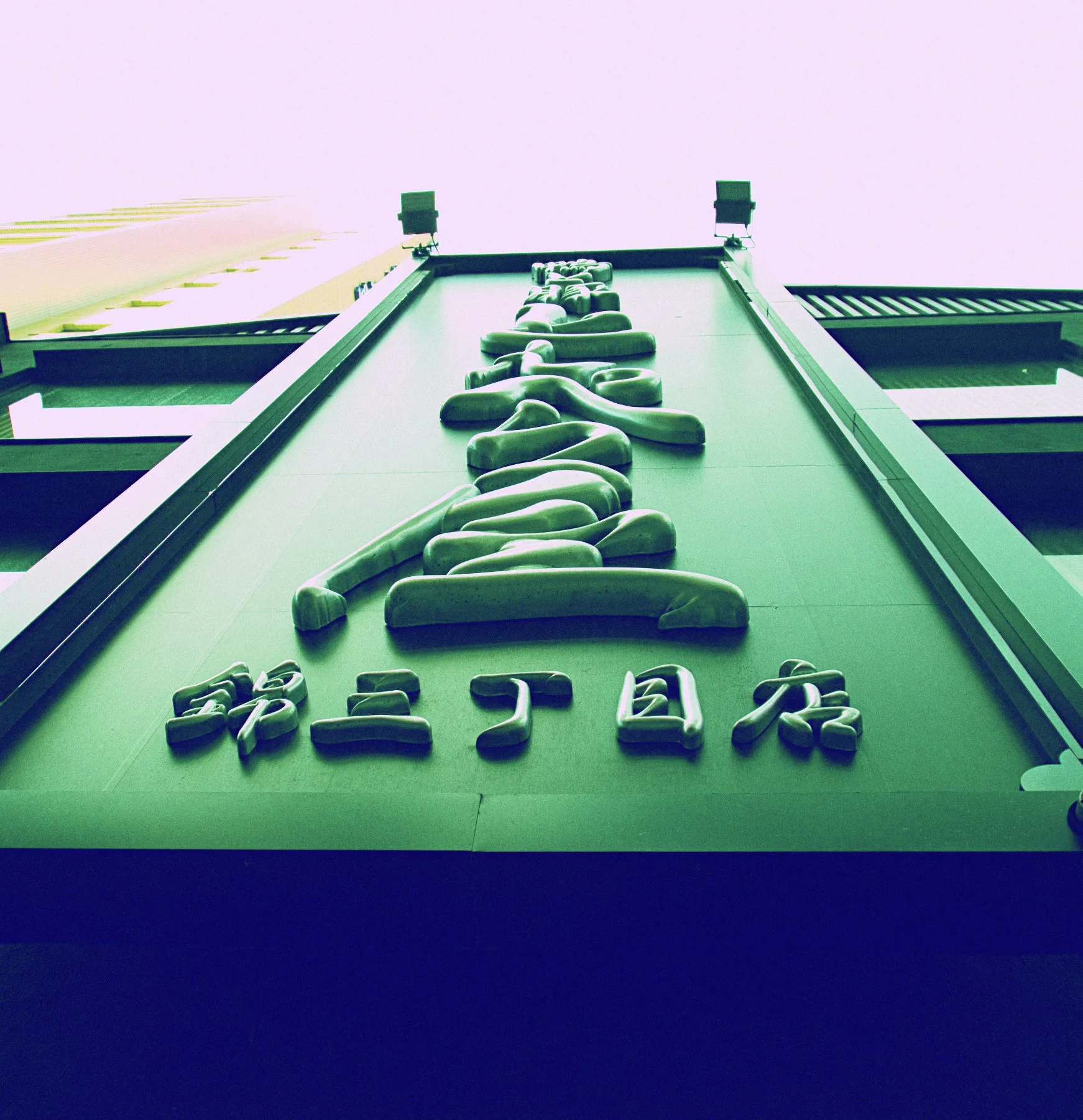 Raised dark characters climb a tapered green facade beneath two small rooftop posts.