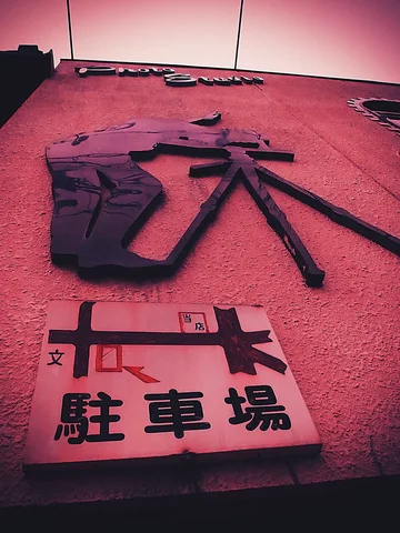Raised dark Japanese characters cover a pink wall above a pale parking sign with a map graphic.