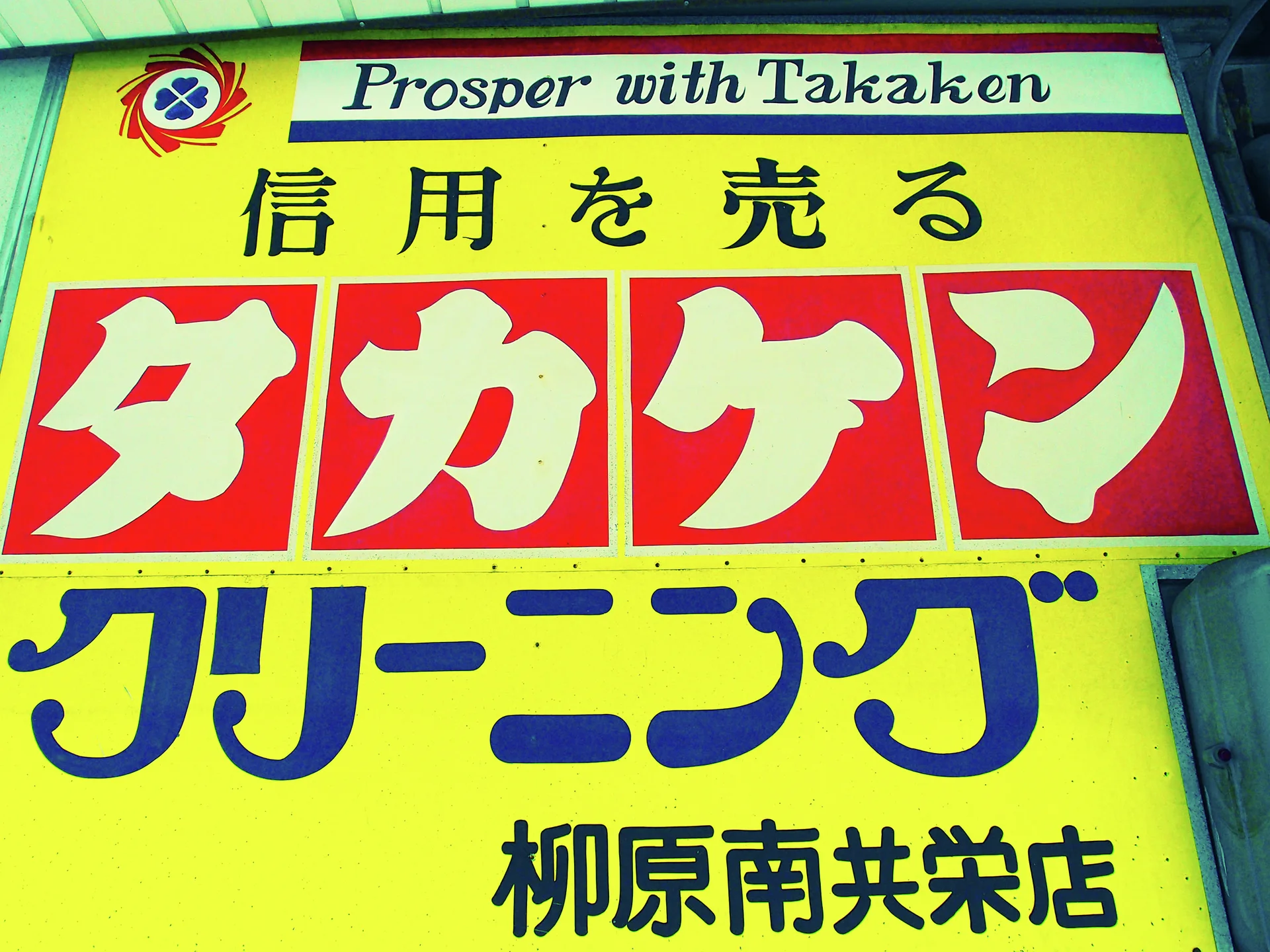 Large red, blue, and black lettering fills a bright yellow cleaning shop sign.