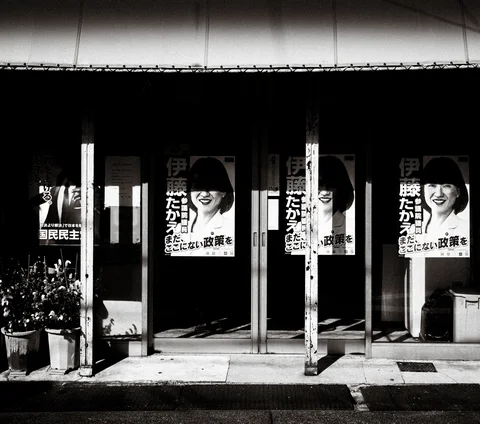 Repeated portrait posters hang between white posts across a dark storefront in black and white.