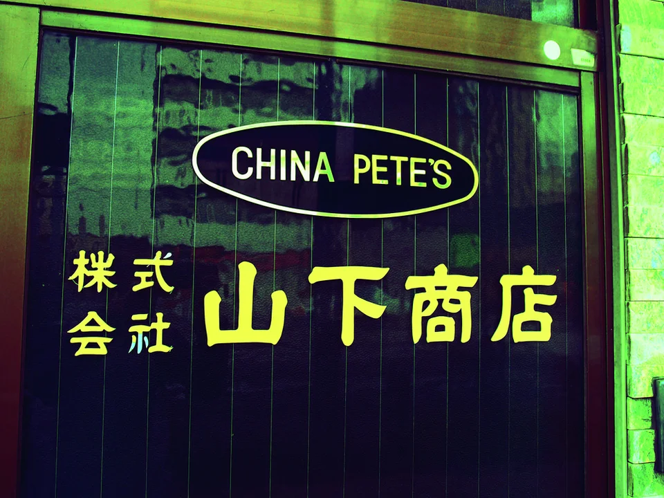 Yellow CHINA PETE窶儡 lettering and Japanese characters fill a dark wooden door beneath a brass-colored frame.