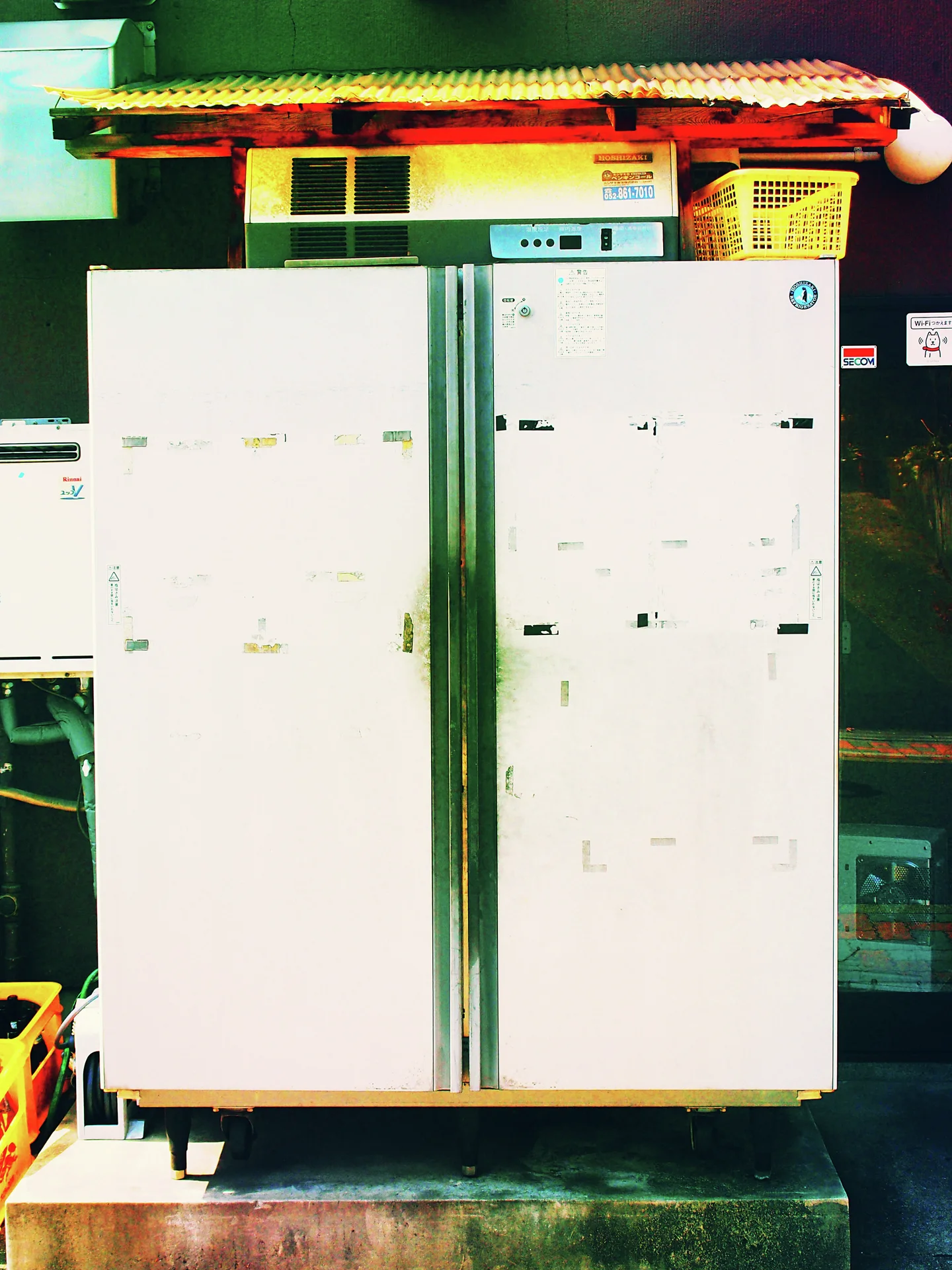 Two tall white metal cabinets stand beneath a small awning beside stacked containers and a yellow basket.