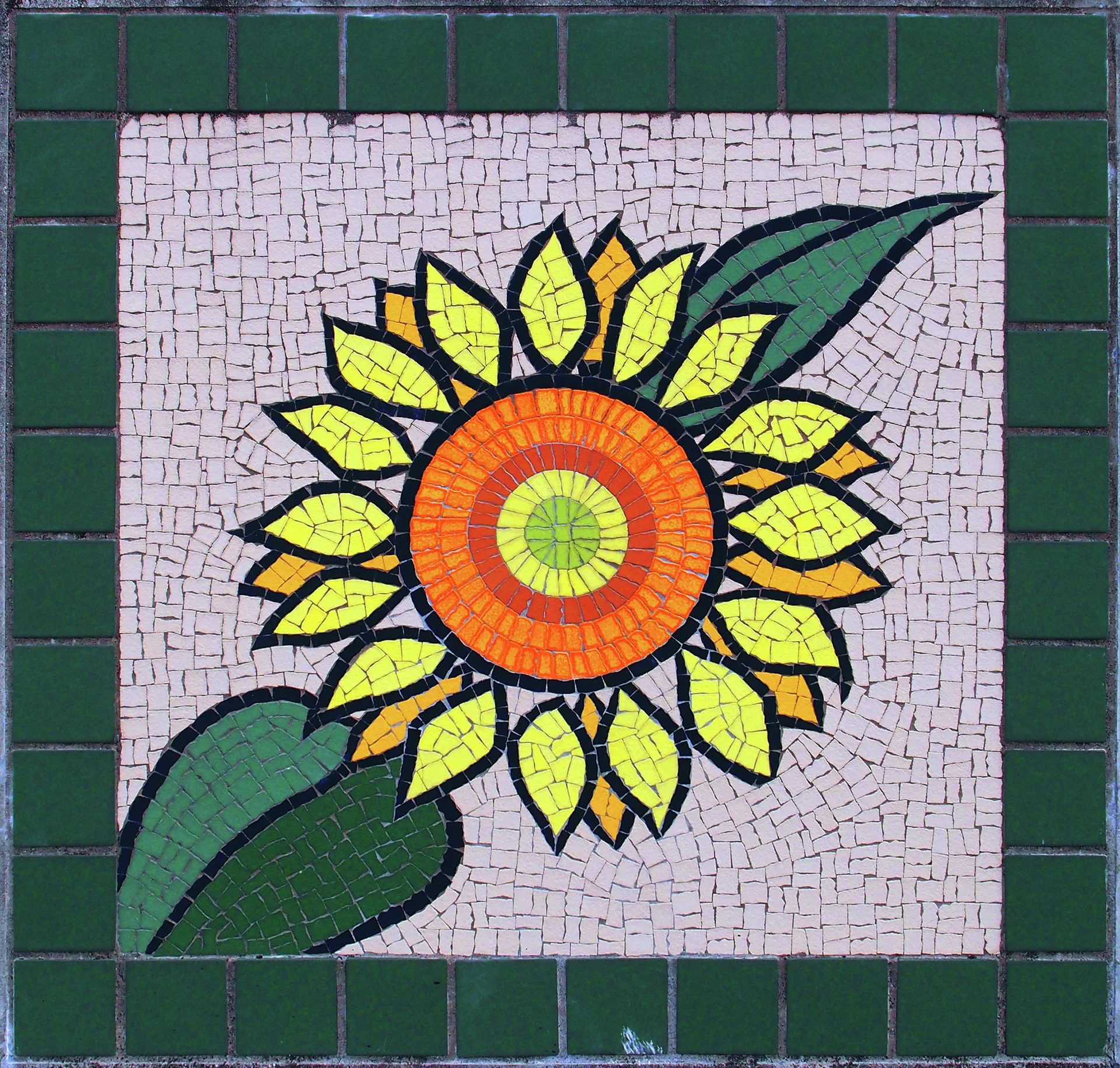 A sunflower mosaic with yellow petals and an orange center sits inside a dark green border.