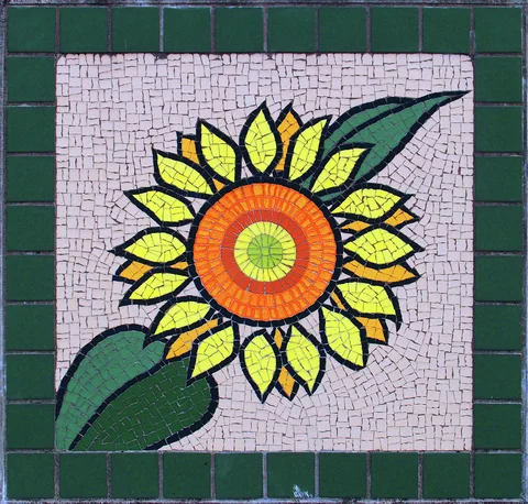 A sunflower mosaic with yellow petals and an orange center sits inside a dark green border.